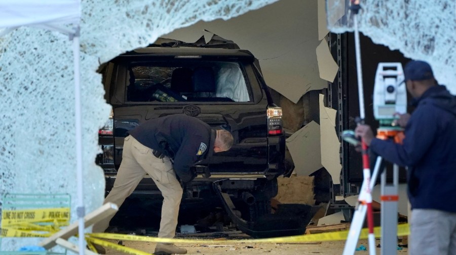 A law enforcement official, center, examines an SUV inside an Apple store, Monday, Nov. 21, 2022, in Hingham, Mass. The crash left a large hole in the glass front of the Apple store.