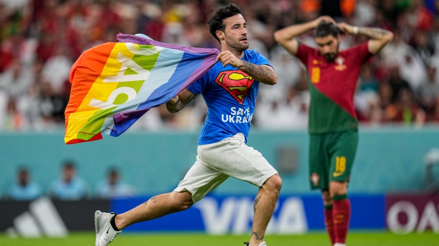 A pitch invader runs across the field with a rainbow flag