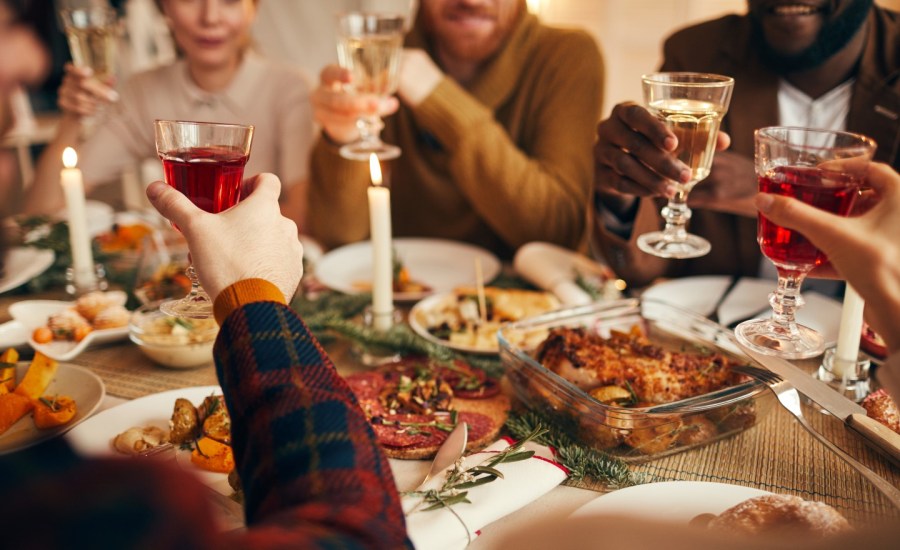 people toasting with drinks in hands at a dinner table with holiday spread