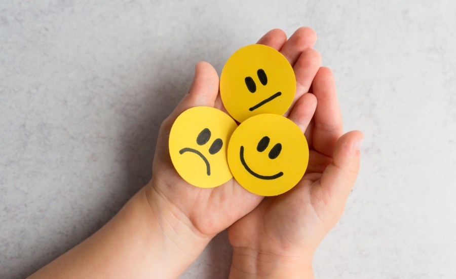 child's hands holding yellow circles showing facial expressions for smiling, sad and neutral