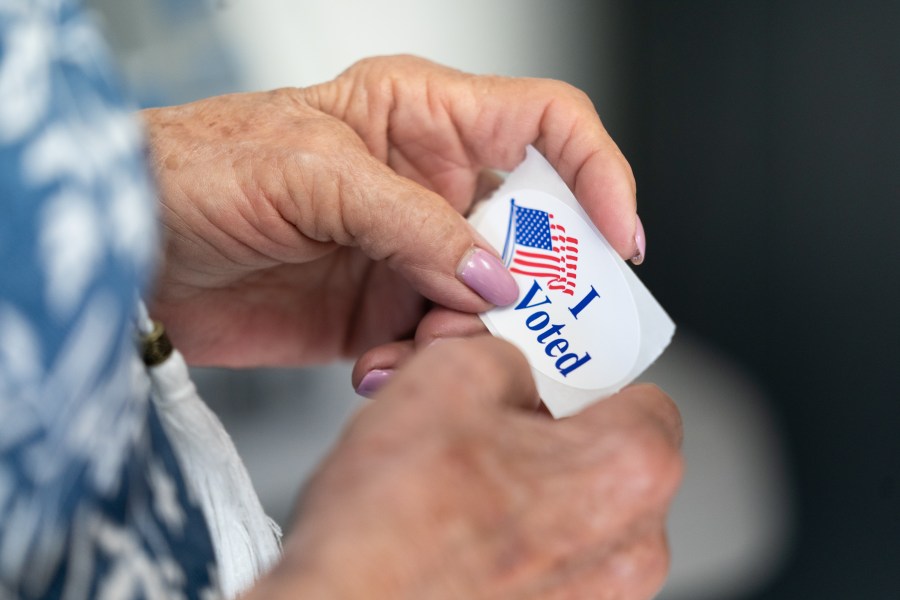 A poll worker holds an "I Voted" sticker with an American fag on it.