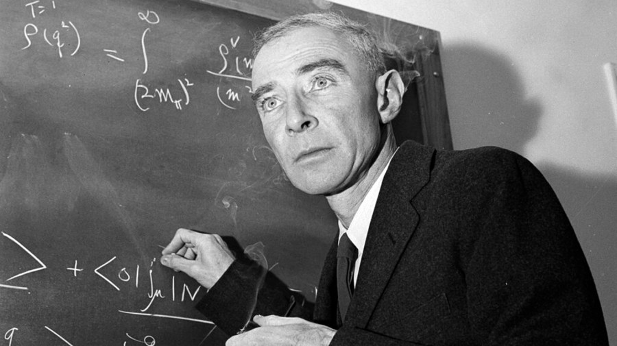 J. Robert Oppenheimer standing in front of a chalkboard.