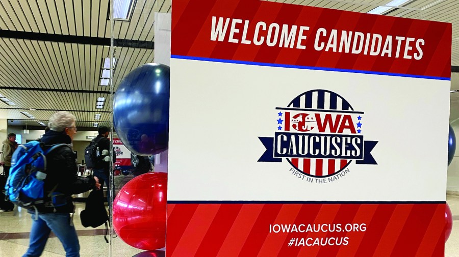 A "Welcome candidates" sign is seen in the spirit of the 2020 Iowa Caucus as a person walks past at Des Moines International Airport