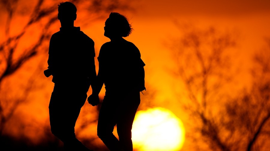 FILE - In this March 10, 2021 file photo, a couple walks through a park at sunset in Kansas City, Mo. U.S.