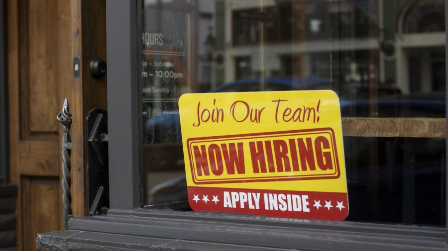 A bright yellow "Now Hiring" sign is displayed in a business's window.