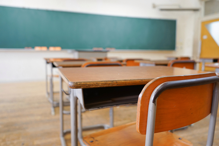 An empty desk is seen in a classroom.