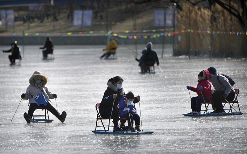 A woman and child push an ice chair across a frozen pond