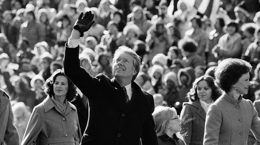 Jimmy Carter waves alongside wife Rosalynn Carter with a crowd of supporters in the background. Black and white photo.