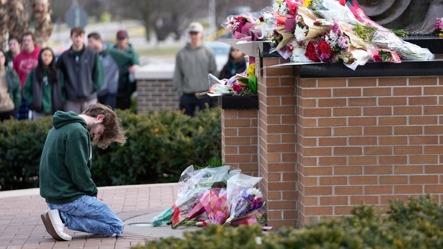 A student kneels where flowers are being left at the Spartan Statue