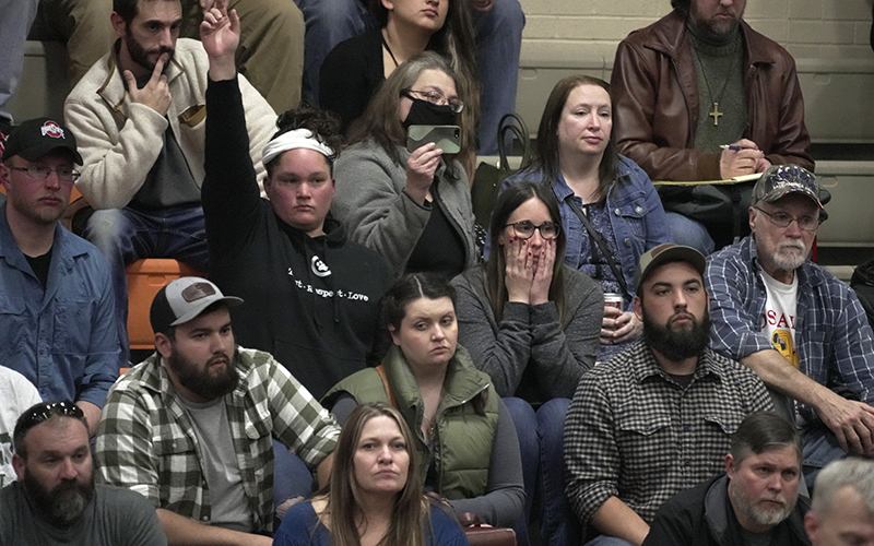 A woman raises her hand with a question during a town hall meeting