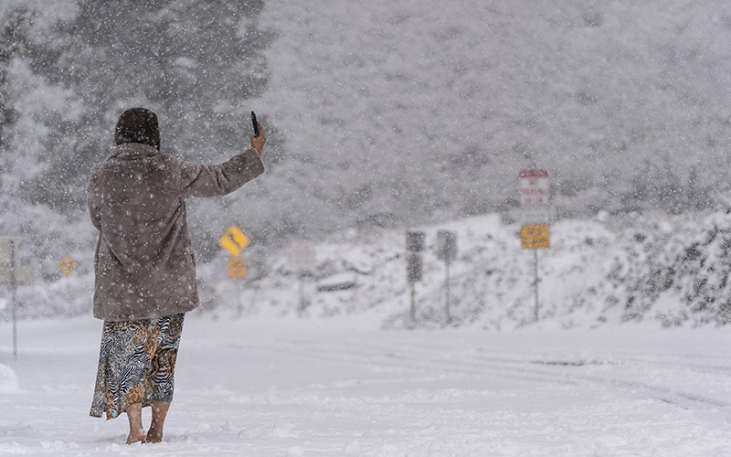 A visitor stands on a snow-covered road while taking a selfie