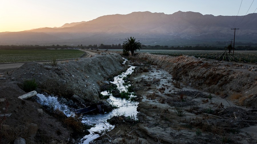 Photo of mostly dry irrigation ditch with sunlit dimming and fog in the distance