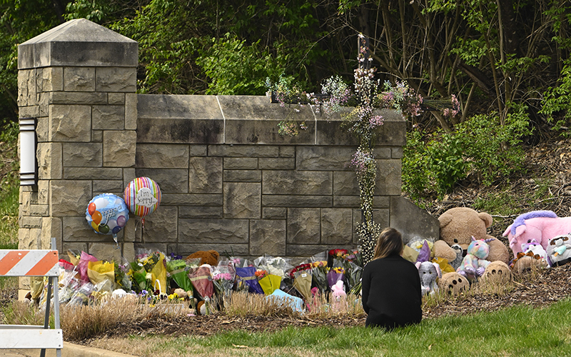 A person kneels in front of an entry to The Covenant School that has become a memorial for shooting victims