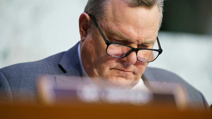 Senator Jon Tester reads something while at a congressional hearing.