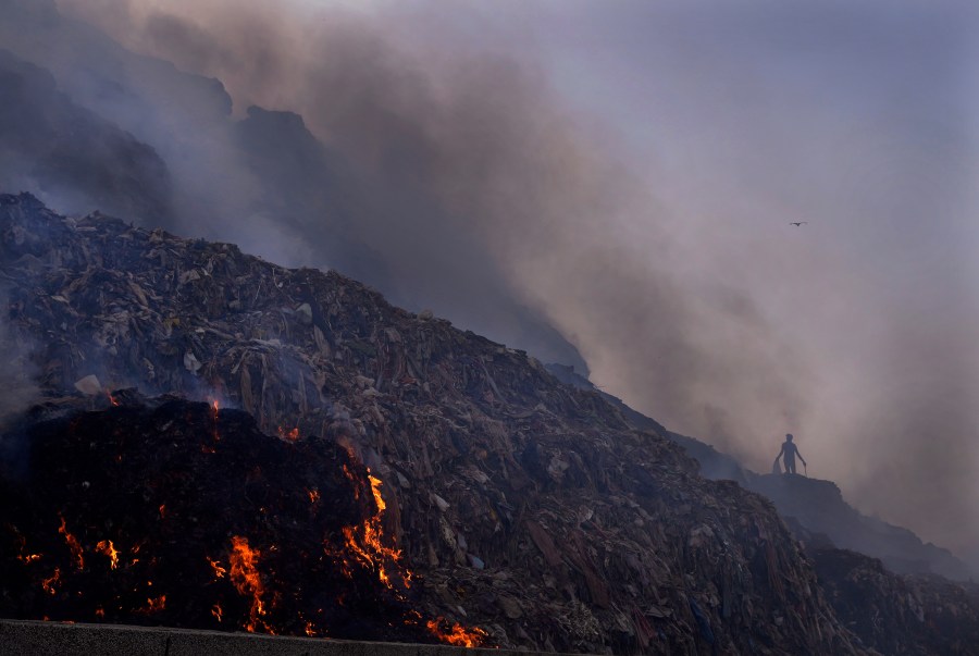 FILE - A person picks through trash for reusable items as a fire rages at the Bhalswa landfill in New Delhi, April 27, 2022. Rising methane levels in the atmosphere in 2022 again played a big part in an overall increase in the greenhouse gases that cause climate change, according to the the National Oceanic and Atmospheric Administration. (AP Photo/Manish Swarup, File)