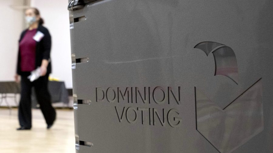 FILE - A worker passes a Dominion Voting ballot scanner while setting up a polling location at an elementary school in Gwinnett County, Ga., outside of Atlanta, on Jan. 4, 2021. The judge presiding over a voting machine company's closely watched defamation lawsuit against Fox News for airing bogus allegations of fraud in the 2020 election indicated Tuesday that he would not allow jurors to hear testimony about specific threats directed at the company. (AP Photo/Ben Gray, File)