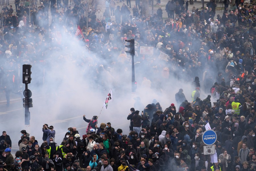 Protesters are seen through tear gas a demonstration, Thursday, April 13, 2023 in Paris. Protesters opposed to President Emmanuel Macron's unpopular plan to raise the retirement age in France marched Thursday in cities and towns around France in a final show of anger before a decision by the Constitutional Council on whether the measure meets constitutional standards. (AP Photo/Thibault Camus)