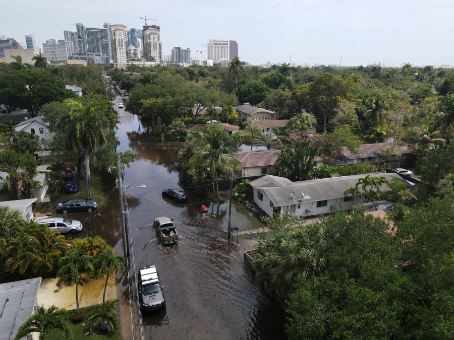 In this photo taken with a drone, trucks and a resident on foot make their way through receding floodwaters in the Sailboat Bend neighborhood of Fort Lauderdale, Fla., Thursday, April 13, 2023. Over 25 inches of rain fell in South Florida since Monday, causing widespread flooding. (AP Photo/Rebecca Blackwell)