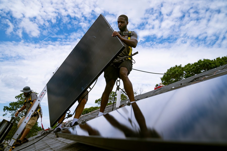 Employees of NY State Solar, a residential and commercial photovoltaic systems company, install an array of solar panels on a roof, Aug. 11, 2022, in the Long Island hamlet of Massapequa, N.Y.