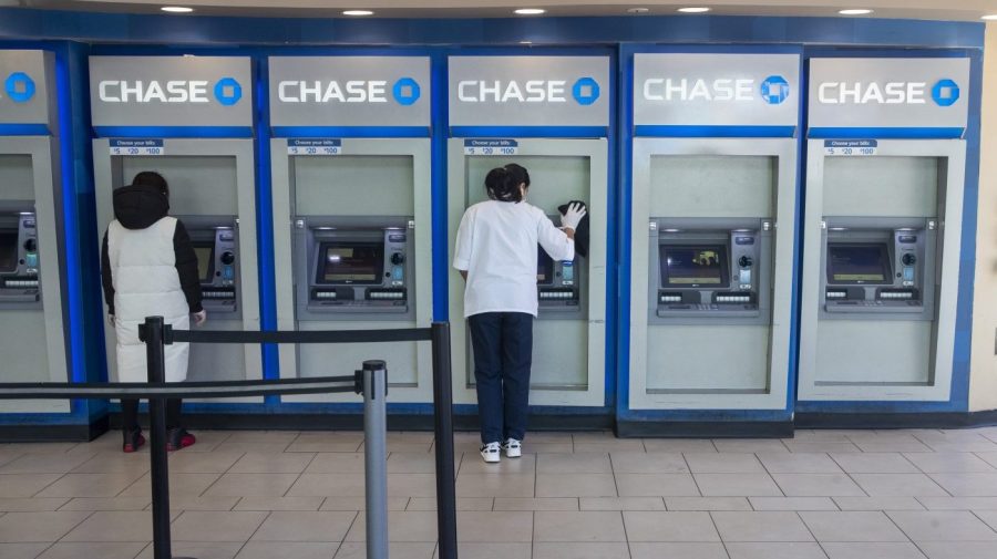 FILE - A worker, right, cleans an ATM as a customer uses another at a Chase branch in the Queens borough of New York on March 24, 2020. Banks are paying up for savers' deposits in a much bigger way than they have in more than a decade, based on the earnings reports from the nation's biggest banks out over the past week. (AP Photo/Mary Altaffer, File)