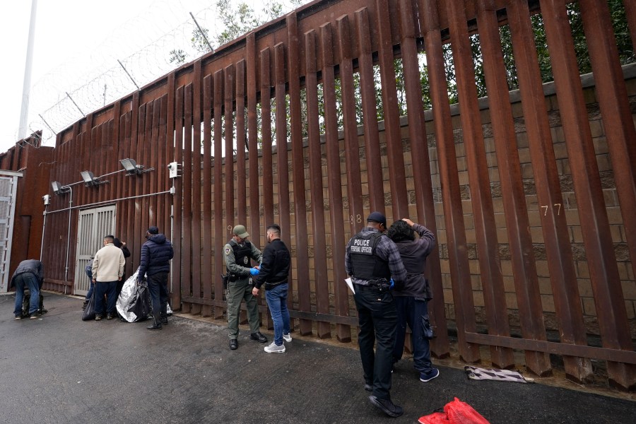 Federal officers remove handcuffs from men before releasing them through a gate in a border wall to Tijuana, Mexico, Wednesday, March 15, 2023, in San Diego. Some asylum-seekers who crossed the border from Mexico are waiting 10 years just for a court date. The Border Patrol released people with notices to appear at a U.S. Immigration and Customs Enforcement office. The move saved the Border Patrol untold hours processing court papers, but it left the job to an agency that had no extra staff for the increased workload. (AP Photo/Gregory Bull)