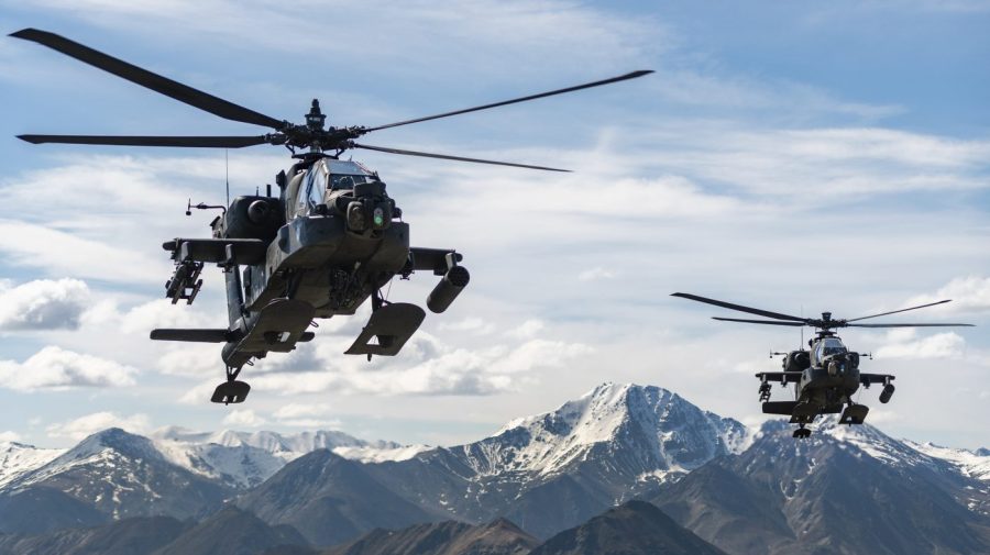 Two Army helicopters fly over a mountain range in Alaska.