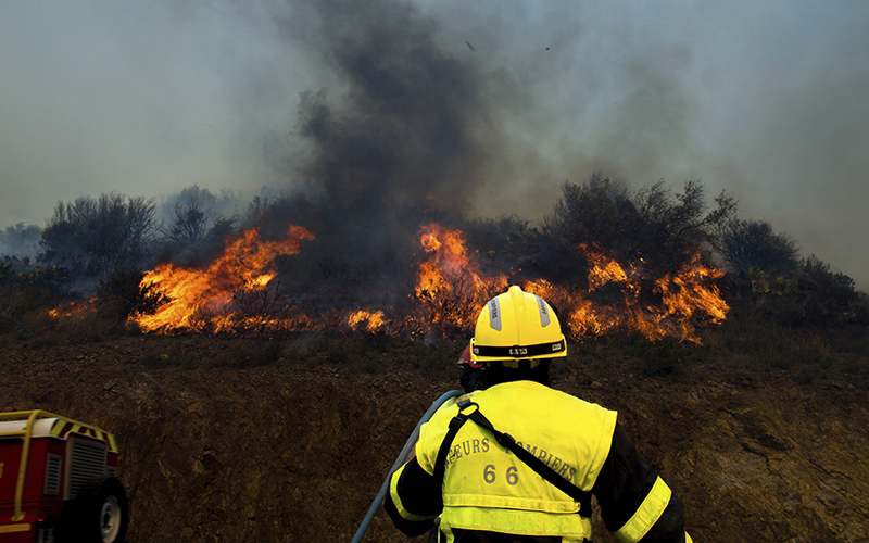 A firefighter looks toward a forest fire in the background as smoke rises into the sky