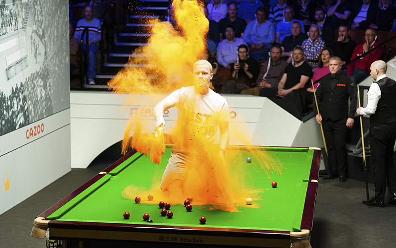 A 'Just Stop Oil' protester jumps on the table and throws orange powder during a snooker match