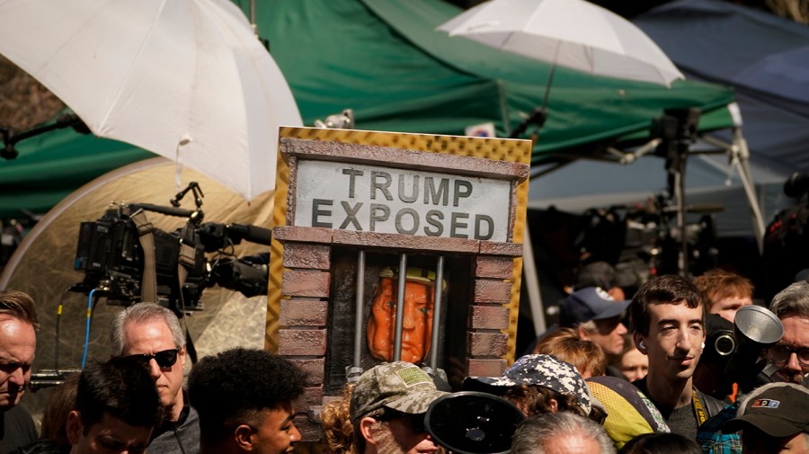 A protester holds a 3D sign depicting Former President Donald Trump behind bars reading "TRUMP EXPOSED"