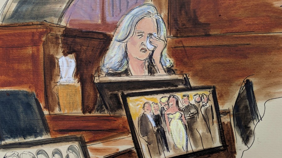 In this courtroom sketch, Natasha Stoynoff weeps on while testifying that Donald Trump pushed himself on to her and made a sexual advance at Mar-a-Lago during her assignment interviewing him and his wife Melania on their one year anniversary, during writer E. Jean Carroll's lawsuit against former President Trump, Wednesday, May 3, 2023, in Manhattan federal court in New York. A photograph of the magazine crew, including Stoynoff, with Donald Trump and Melania is displayed on a computer monitor. Trump has denied that he ever tried to kiss Stoynoff. (Elizabeth Williams via AP)