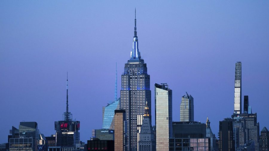 The Empire State Building glows blue during dusk against the New York City skyline.