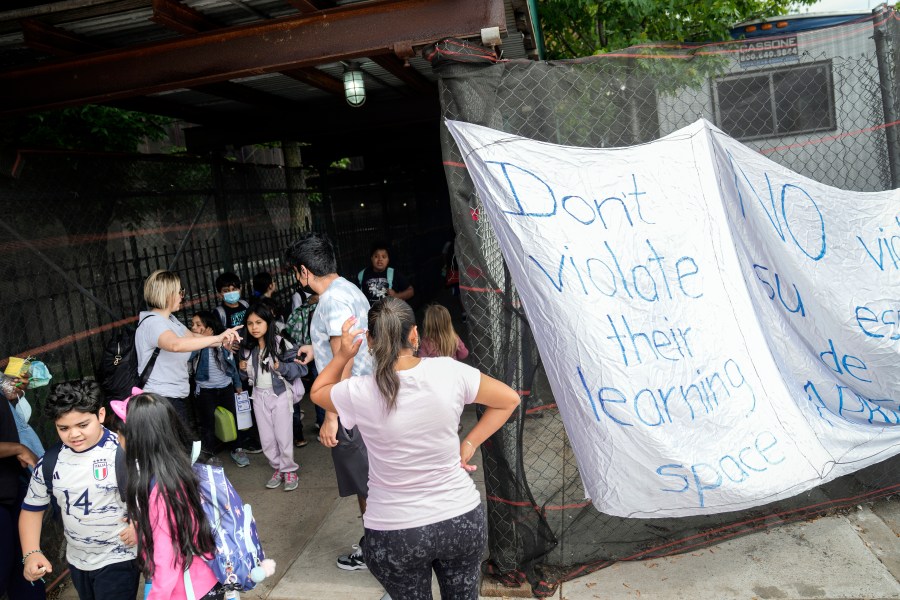 Students exit P.S. 172 after classes end for the day as a protest sign is displayed outside the school, Tuesday, May 16, 2023, in New York. New York City Mayor Eric Adam's plan to temporarily house immigrants in the school's gymnasium has frustrated some community members who protested outside the building earlier in the day. (AP Photo/John Minchillo)