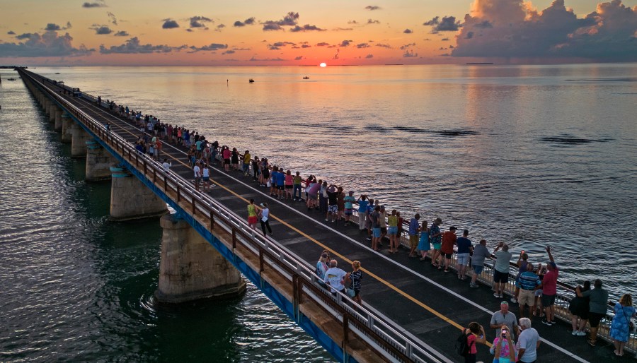 In this aerial photo provided by the Florida Keys News Bureau, attendees watch and toast the sunset at a Florida Keys bicentennial celebration, Friday, May 19, 2023, on the restored Old Seven Mile Bridge in Marathon, Fla. The sunset gathering was among a series of Keys events being staged to mark the 200th anniversary, on July 3, of the Florida Territorial Legislature's 1823 founding of Monroe County, containing the entire island chain. The old bridge was originally part of Henry Flagler's Florida Keys Over-Sea Railroad completed in 1912, and is now closed to vehicles but open to pedestrians and bicycles. (Andy Newman/Florida Keys News Bureau via AP)