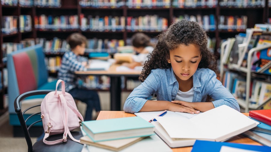 african american schoolgirl reading book in library