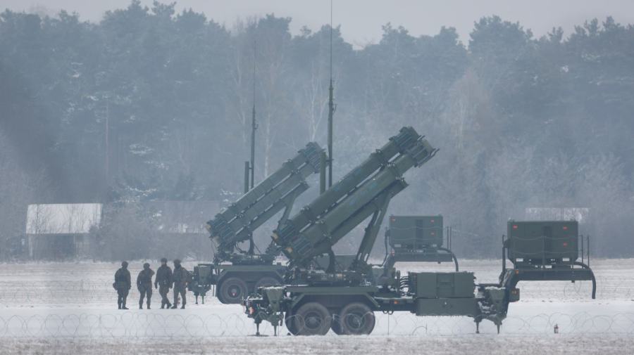 Patriot missile launchers are seen on a snowy ground as workers stand nearby.