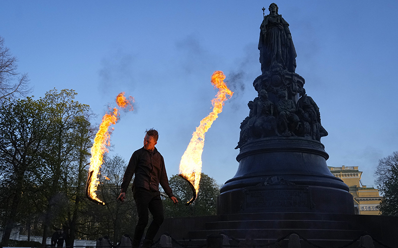 A street performer dances with fire next to the statue