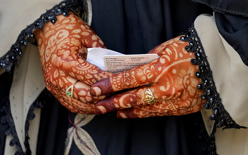 A woman with her hands decorated with henna holds her voter identity card