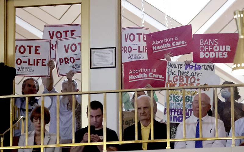 Protesters on both sides of the abortion issue hold signs looking into the North Carolina House as members debate