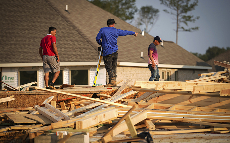 Men gather tools from a scene where a house under construction collapsed from high winds