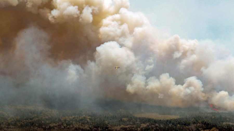 In this aerial image, an aircraft, center, flies near a wildfire burning near Barrington Lake in Shelburne County, Nova Scotia, on Wednesday, May 31, 2023. (Communications Nova Scotia/The Canadian Press via AP)