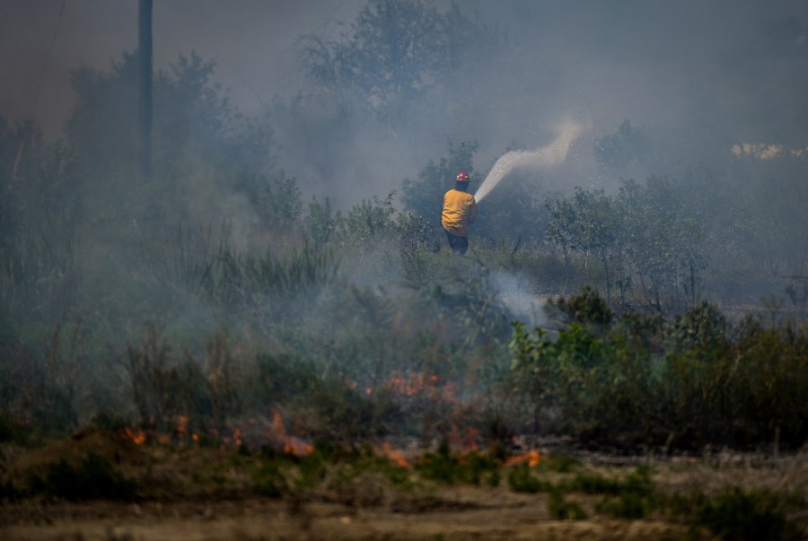 A firefighter directs water on a grass fire on an acreage behind a residential property in Kamloops, British Columbia, Monday, June 5, 2023. No structures were damaged but firefighters had to deal with extremely windy conditions while putting out the blaze. (Darryl Dyck/The Canadian Press via AP)