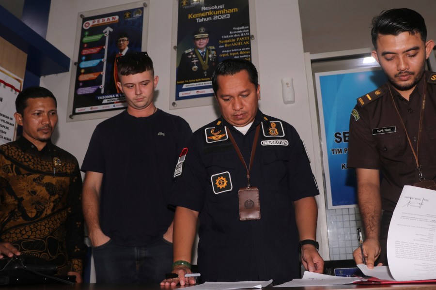 Bodhi Mani Risby-Jones from Queensland, Australia, second left, looks on as prosecutor and immigration officials sign his transfer documents at the local immigration office in Meulaboh, Aceh, Indonesia on Wednesday, June 7, 2023. The Australian surfer who was jailed for attacking several people while drunk and naked in Indonesia's deeply conservative Muslim province of Aceh will be deported back to his country after he agreed to apologize and pay compensation, officials said Wednesday. (AP Photo/Sultan Ikbal Abiyyu)