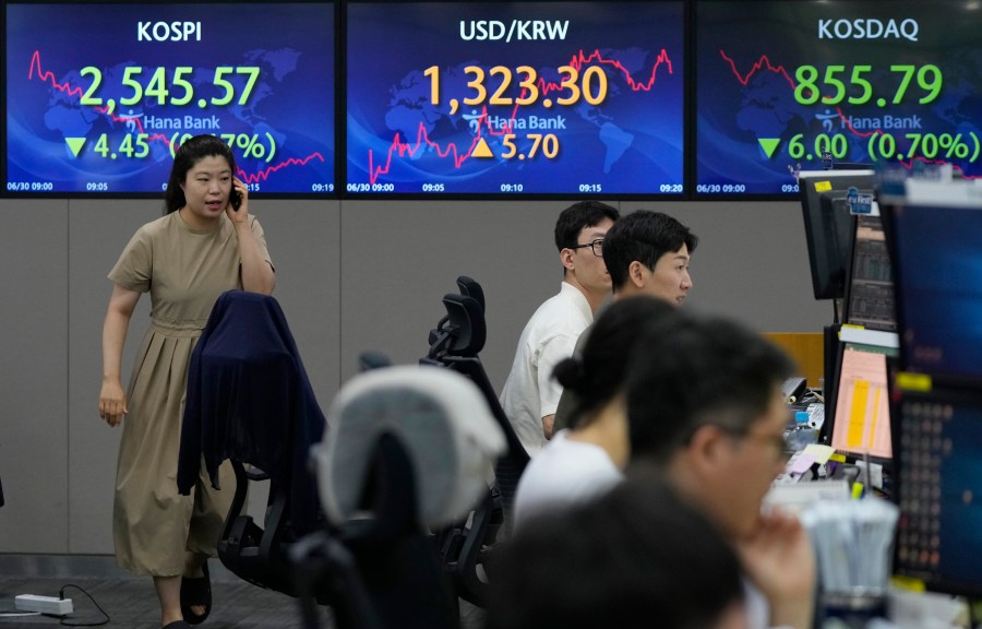 A currency trader passes by screens showing the Korea Composite Stock Price Index (KOSPI), top left, and the foreign exchange rate between U.S. dollar and South Korean won, top center, at the foreign exchange dealing room of the KEB Hana Bank headquarters in Seoul, South Korea, Friday, June 30, 2023. Shares were mixed Friday in Asia after China reported slower factory activity in June due to weaker consumer spending and export demand. (AP Photo/Ahn Young-joon)