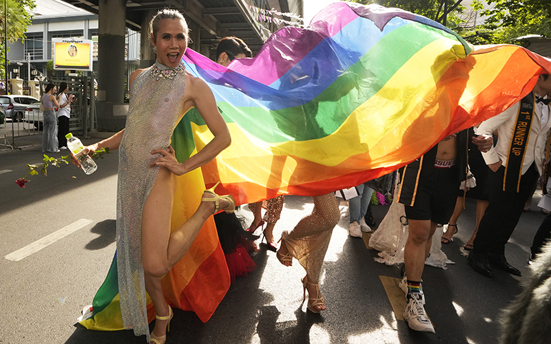 A participant poses as a rainbow flag unfurls behind them during a Pride Parade