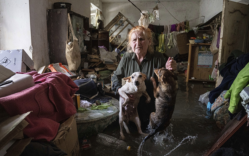 A resident holds her dogs as she stands in her home that was flooded roughly knee-deep under water after the Kakhovka Dam blew up