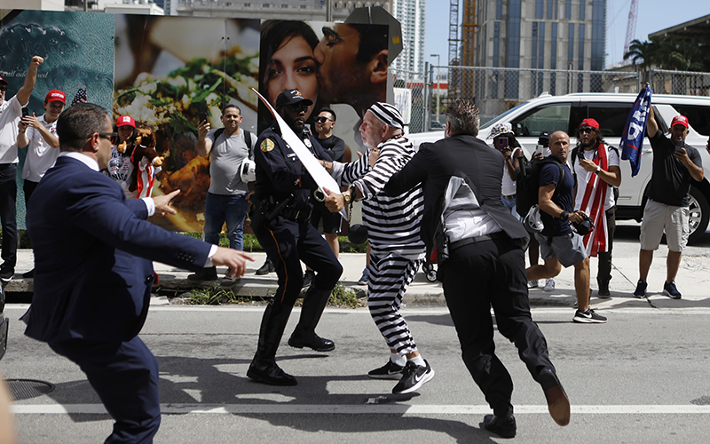 A protester in a black and white striped costume grapples with security forces in the street