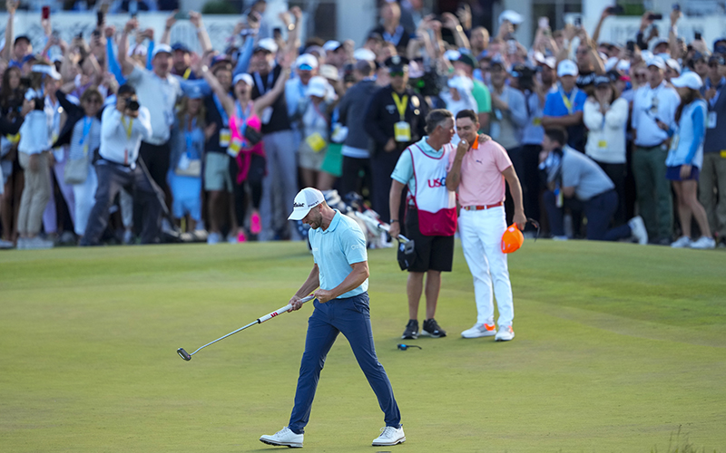 Wyndham Clark celebrates on the 18th hole after winning the U.S. Open golf tournament while a crowd behind him cheers