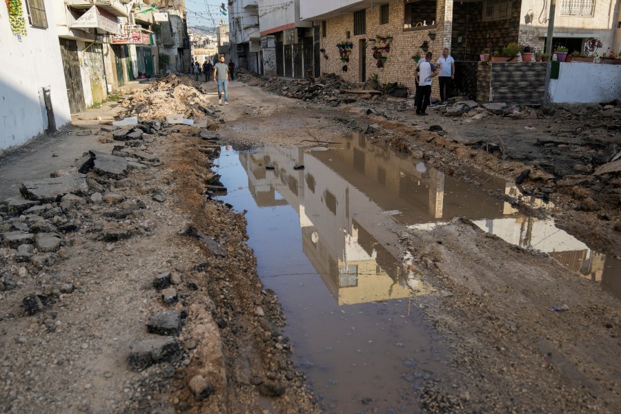 Palestinians walk on a damaged road in the Jenin refugee camp in the West Bank, Wednesday, July 5, 2023, after the Israeli army withdrew its forces from the militant stronghold. The withdrawal of troops from the camp ended an intense two-day operation that killed at least 13 Palestinians, drove thousands of people from their homes and left a wide swath of damage in its wake. One Israeli soldier was also killed. (AP Photo/Nasser Nasser)