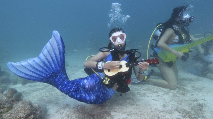 In this photo provided by the Florida Keys News Bureau, Tamara Bredova, left, costumed as a mermaid, pretends to play a ukulele underwater, Saturday, July 8, 2023, while Kelly Angel, right, strokes a faux guitar at the Lower Keys Underwater Music Festival in the Florida Keys National Marine Sanctuary near Big Pine Key, Fla. Several hundred divers and snorkelers submerged along a portion of the continental United States' only living coral barrier reef to listen to a local radio station's four-hour broadcast, piped beneath the sea to promote coral reef preservation. Kelly Angel is at right. (Frazier Nivens/Florida Keys News Bureau via AP)