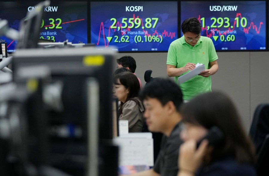 A currency trader passes by screens showing the Korea Composite Stock Price Index (KOSPI), top center, and the foreign exchange rate between U.S. dollar and South Korean won, top right, at the foreign exchange dealing room of the KEB Hana Bank headquarters in Seoul, South Korea, Wednesday, July 12, 2023. Asian shares were mostly higher on Wednesday after stocks advanced on Wall Street as investors awaited an update on U.S. inflation that will hopefully show a smaller increase in pain for everyone.(AP Photo/Ahn Young-joon)